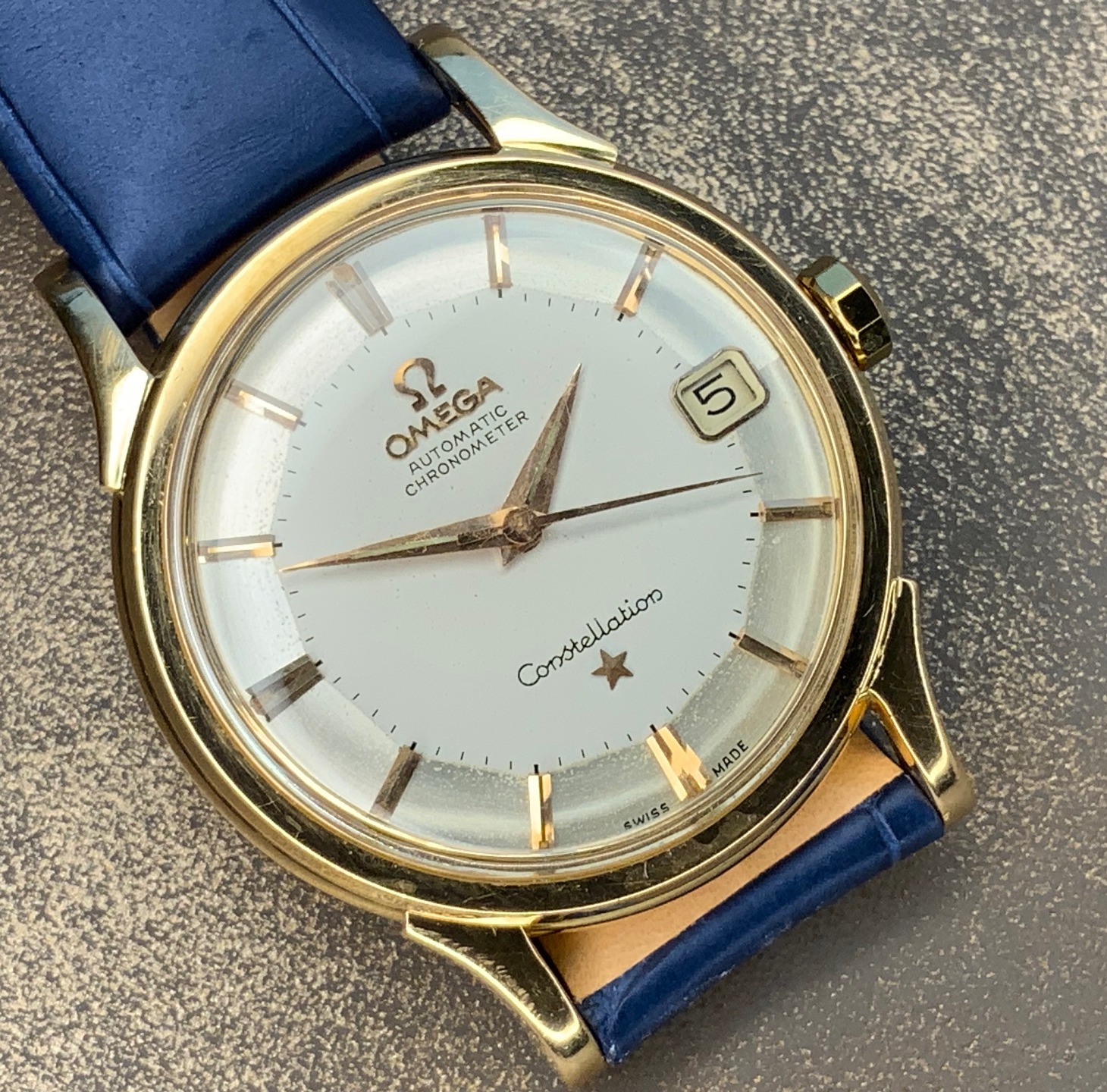Omega Constellation Automatic Chronometer in 18k gold with silver pie-pan dial and deep blue leather strap.